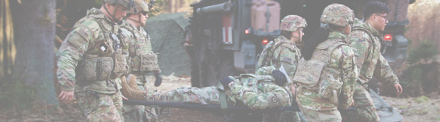 Six US Army soldiers in camouflage uniforms carry a simulated casualty on a litter during a training exercise.