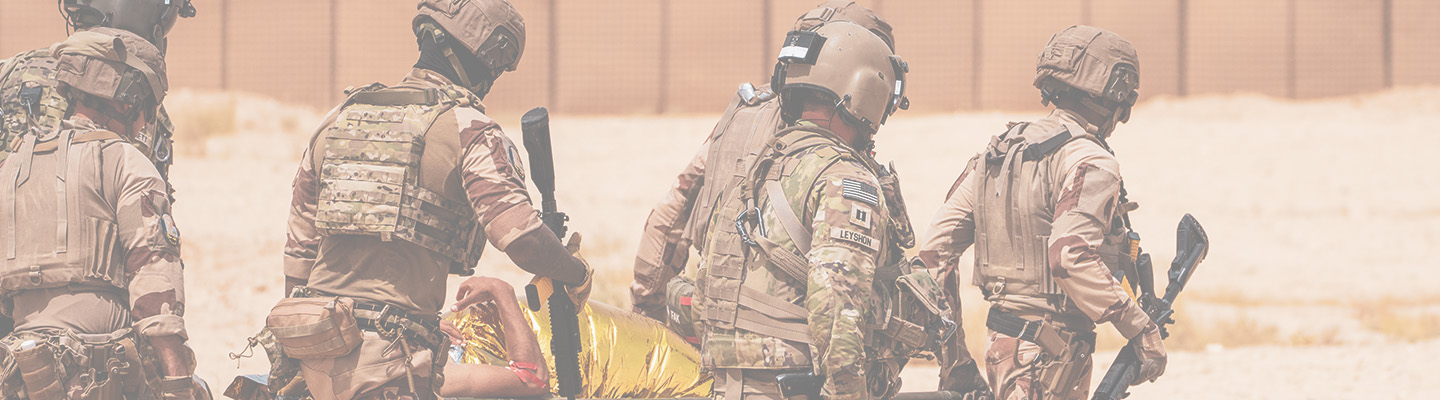 Six US Army soldiers in camouflage uniforms carry a simulated casualty on a litter during a training exercise.