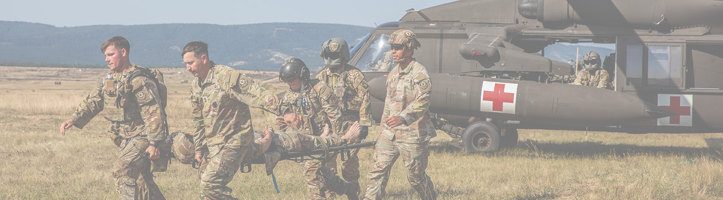 Five US Army soldiers in camouflage uniforms carry a simulated casualty on a litter during a training exercise.